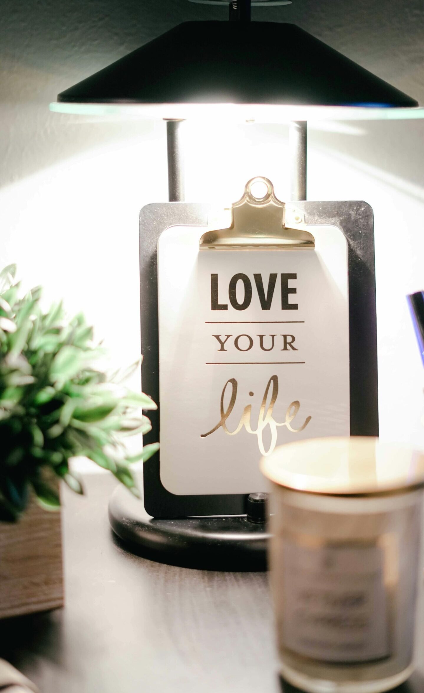 A warmly lit desk setup featuring a lamp, inspirational clipboard, and decor for a cozy ambiance.
