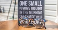 Eyeglasses resting on a table in front of a motivational quote sign, emphasizing positivity.